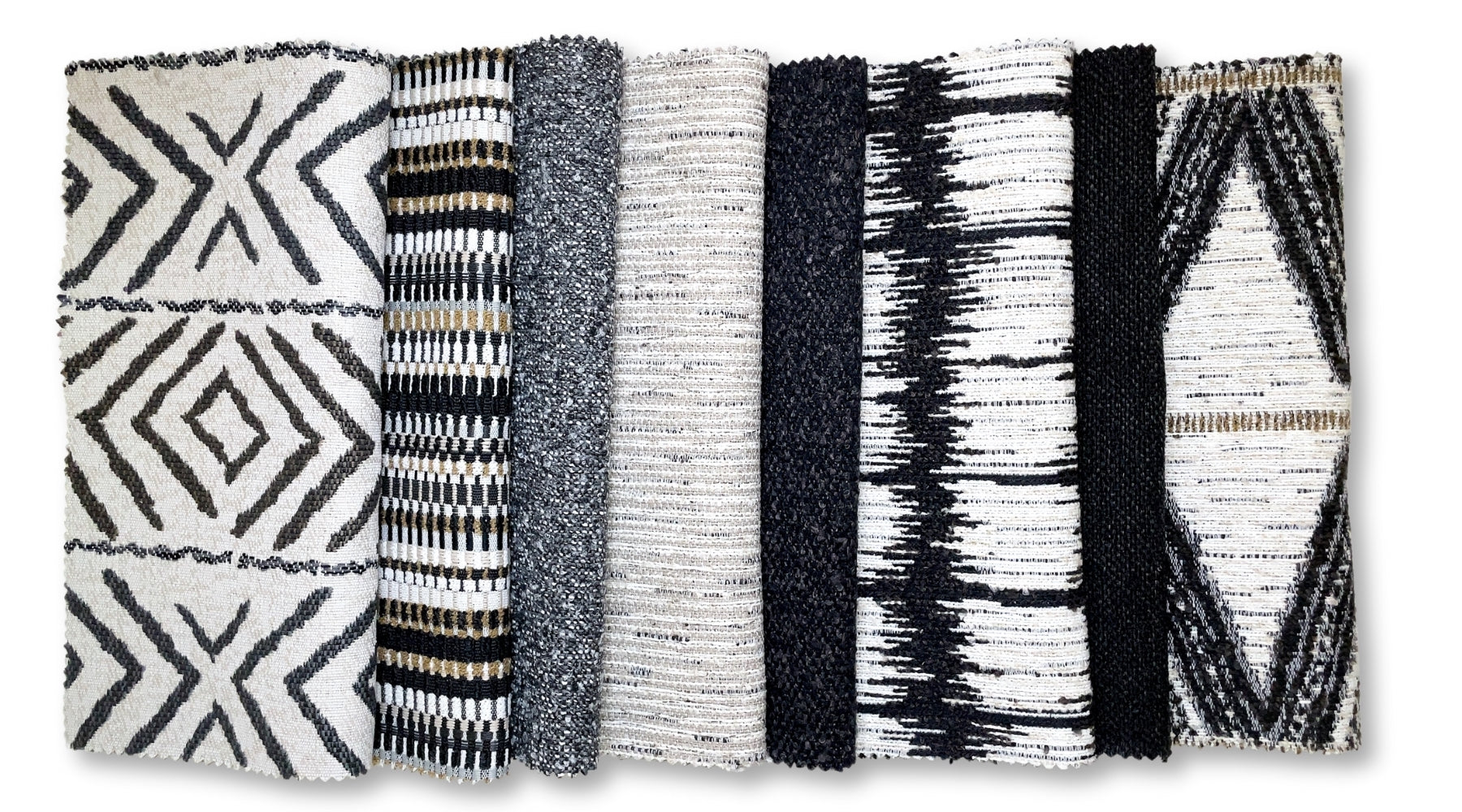 An array of fabric swatches showcasing a variety of textures and patterns in black, white, and gray tones. From left to right: a bold geometric pattern, a textured solid gray, a narrow stripe, a speckled tweed, a darker solid, a high-contrast ikat design, and a fabric featuring a tribal-inspired print with gold accents.