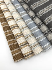 Assorted Revolution Performance Upholstery Fabric swatches in the Billie pattern arranged in a fanned layout, showcasing vertical stripe designs across multiple neutral colorways. Each swatch displays Billie’s evenly spaced stripes with subtle irregularity, highlighting a woven texture with soft tonal variation and a tactile, fabric-forward surface.
