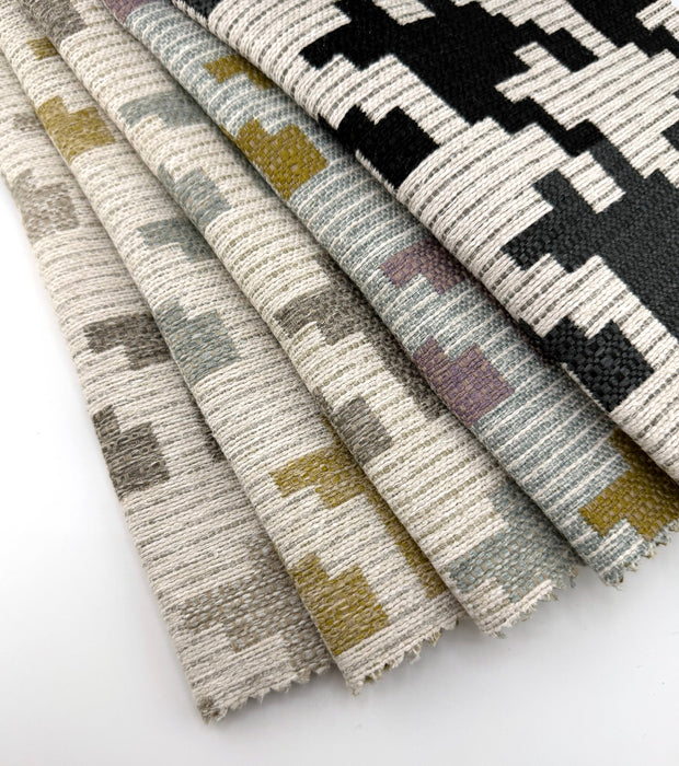 Assorted Revolution Performance Upholstery Fabric swatches in pattern Blass, arranged in a fanned layout to show the interlocking modern shapes across all colorways—Berber, Ebony, Powder, Meadow, and Capri. Each swatch displays the woven texture with subtle tonal variation, highlighting the durability and contemporary geometric design.