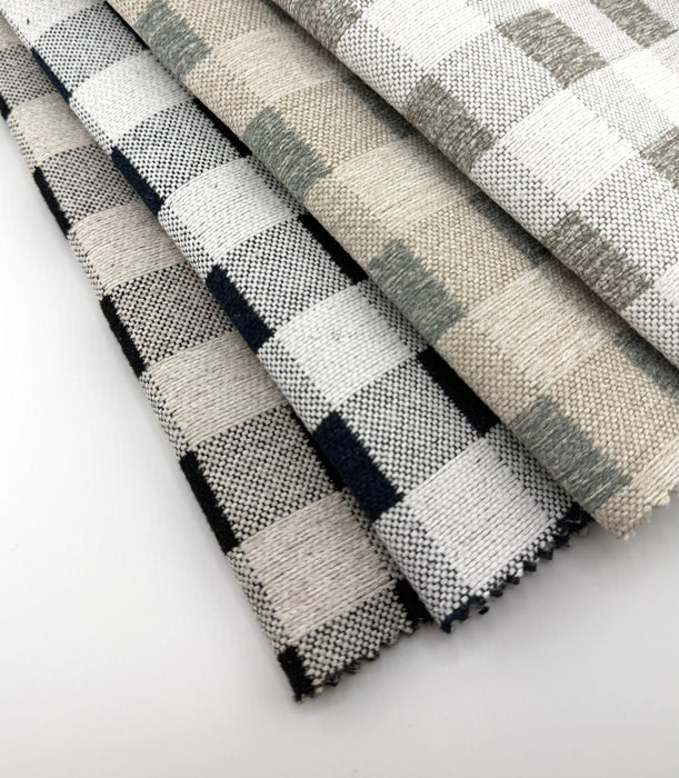 Fanned swatches of Revolution Performance Fabric, pattern Brompton in Indigo, Black, Taupe, and Spa, showcasing classic buffalo check upholstery fabric in versatile neutral and blue-green colorways.