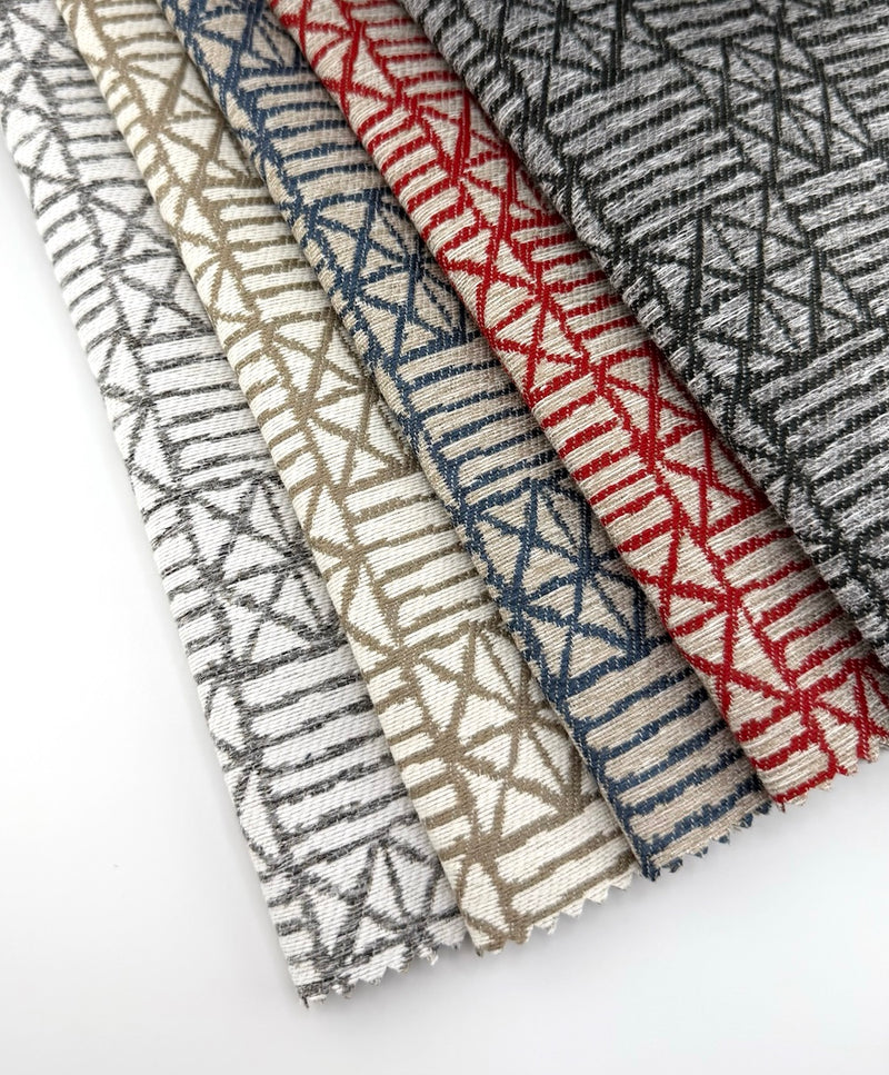 Assorted Revolution Performance Upholstery Fabric swatches in the Delgado pattern arranged in a fanned layout, showcasing multiple neutral and accent colorways with woven geometric block motifs and a textured, durable upholstery finish.