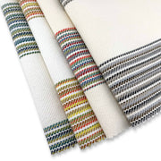 Assorted Revolution Performance Fabric swatches from the Gracias collection arranged in a fanned layout, featuring an ivory woven base accented with multicolored vertical stripes in blue, green, coral, yellow, and neutral tones, showcasing the collection’s textured, durable upholstery construction.