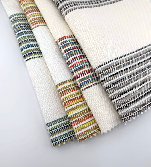 Assorted Revolution Performance Fabric swatches from the Gracias collection arranged in a fanned layout, featuring an ivory woven base accented with multicolored vertical stripes in blue, green, coral, yellow, and neutral tones, showcasing the collection’s textured, durable upholstery construction.