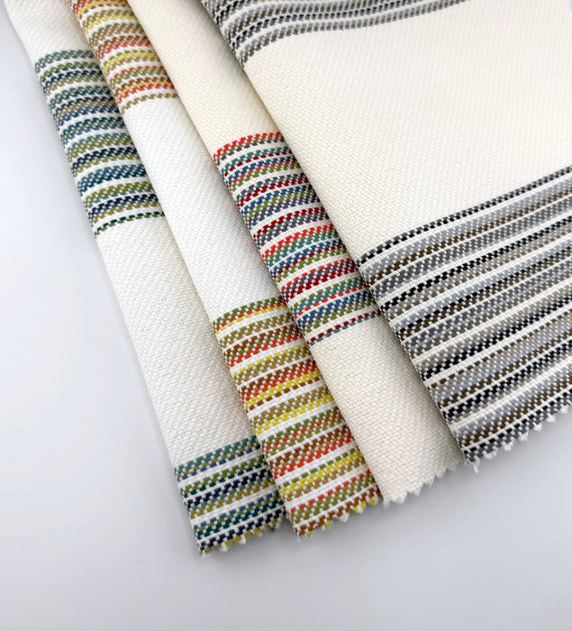 Assorted Revolution Performance Fabric swatches from the Gracias collection arranged in a fanned layout, featuring an ivory woven base accented with multicolored vertical stripes in blue, green, coral, yellow, and neutral tones, showcasing the collection’s textured, durable upholstery construction.