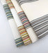 Assorted Revolution Performance Fabric swatches from the Gracias collection arranged in a fanned layout, featuring an ivory woven base accented with multicolored vertical stripes in blue, green, coral, yellow, and neutral tones, showcasing the collection’s textured, durable upholstery construction.