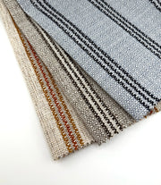 Assorted Revolution Performance Upholstery Fabric swatches from the High Society collection arranged in a fanned layout. Each swatch displays High Society’s tightly woven texture with clean, evenly spaced vertical stripes in coordinated neutral and accent colorways, including brown, lapis blue, and terra cotta tones.