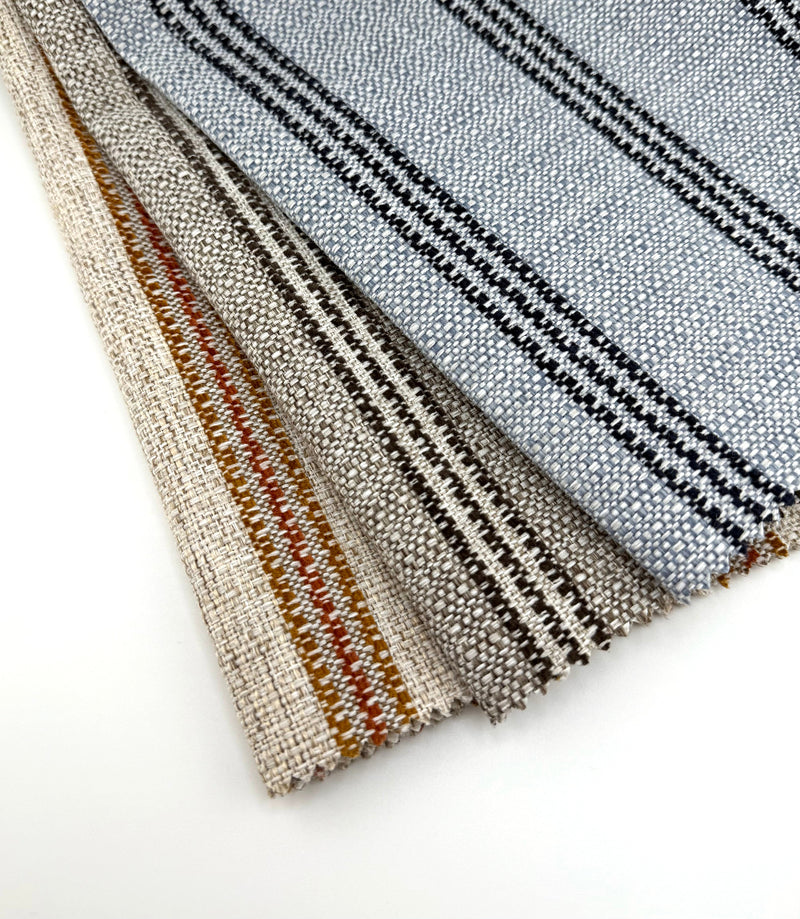 Assorted Revolution Performance Upholstery Fabric swatches from the High Society collection arranged in a fanned layout. Each swatch displays High Society’s tightly woven texture with clean, evenly spaced vertical stripes in coordinated neutral and accent colorways, including brown, lapis blue, and terra cotta tones.