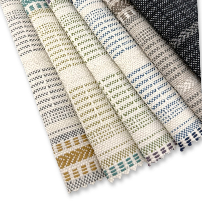 Assorted Revolution Performance Upholstery Fabric swatches arranged in a fanned layout. Each swatch displays the Lloyd collection’s woven stripe texture with subtle tonal variation in soft neutrals, greens, blues, warm gold, and charcoal, highlighting the fabric’s crisp structure and refined surface detail.