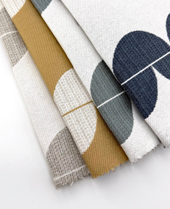 Assorted Revolution Performance Upholstery Fabric swatches in the Lunar pattern, arranged in a fanned layout, featuring modern geometric crescent shapes in coordinated neutral and earthy colorways on an ivory ground, showcasing a woven texture designed for durable, high-performance upholstery applications.