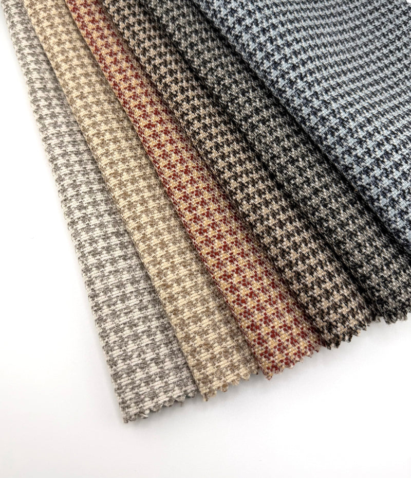 Assorted Revolution Performance Upholstery Fabric swatches from the Menswear collection arranged in a fanned layout. Each swatch displays Menswear’s fine-scale woven surface inspired by classic houndstooth, with tightly interlocked yarns and subtle tonal variation across neutral and tailored colorways.