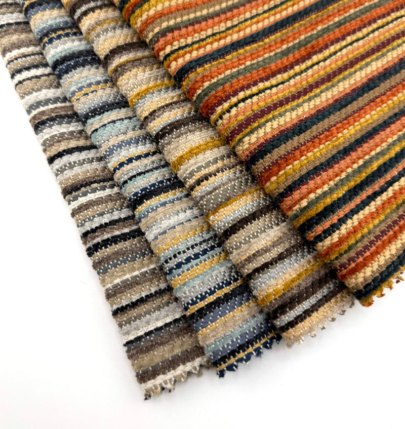 Assorted Revolution Performance Upholstery Fabric swatches from the Mixology collection arranged in a fanned layout. Each swatch displays Mixology’s narrow vertical stripe pattern with a varied, softly ribbed woven texture and subtle height variation, creating layered tonal contrast across the surface.