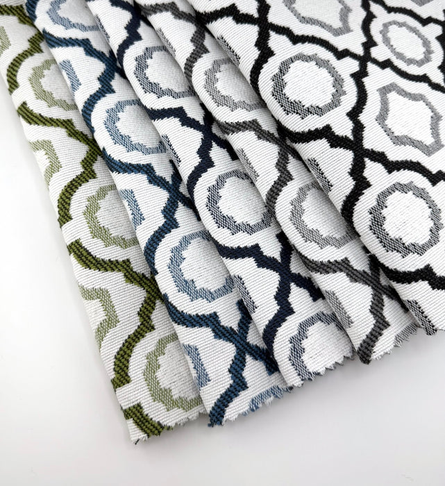 Assorted Revolution Performance Fabric swatches in the Savannah pattern arranged in a fanned layout, showcasing green, navy, blue, grey, and black geometric lattice designs woven over an ivory base for durable, high-performance upholstery applications.