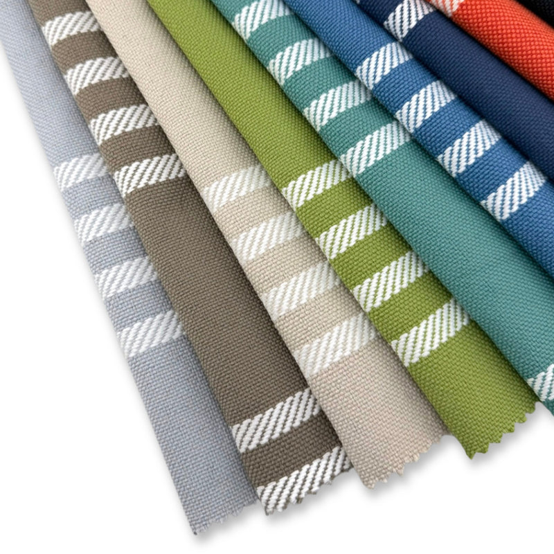 Assorted Revolution Performance Fabric swatches in the Shade pattern, arranged in a fanned layout showcasing multiple colorways including aqua, denim, navy, flame, chive, taupe, aluminum, sand, and carbon. Each swatch features vertical woven stripes with crisp white rope-inspired accents, highlighting the texture and durability of this high-performance striped upholstery fabric.