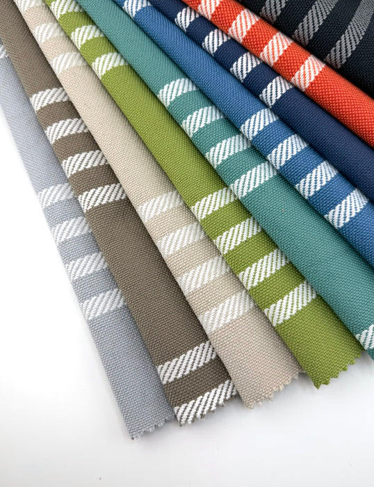 Assorted Revolution Performance Fabric swatches in the Shade pattern, arranged in a fanned layout showcasing multiple colorways including aqua, denim, navy, flame, chive, taupe, aluminum, sand, and carbon. Each swatch features vertical woven stripes with crisp white rope-inspired accents, highlighting the texture and durability of this high-performance striped upholstery fabric.