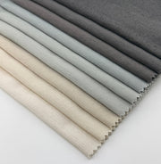 Assorted Revolution Performance Upholstery Fabric swatches from the Shelter collection arranged in a fanned layout, showing multiple colors including ivory, cream, beige, stone, light grey, silver grey, and charcoal variations. Each swatch displays Shelter’s smooth, tightly woven texture with subtle tonal variation.