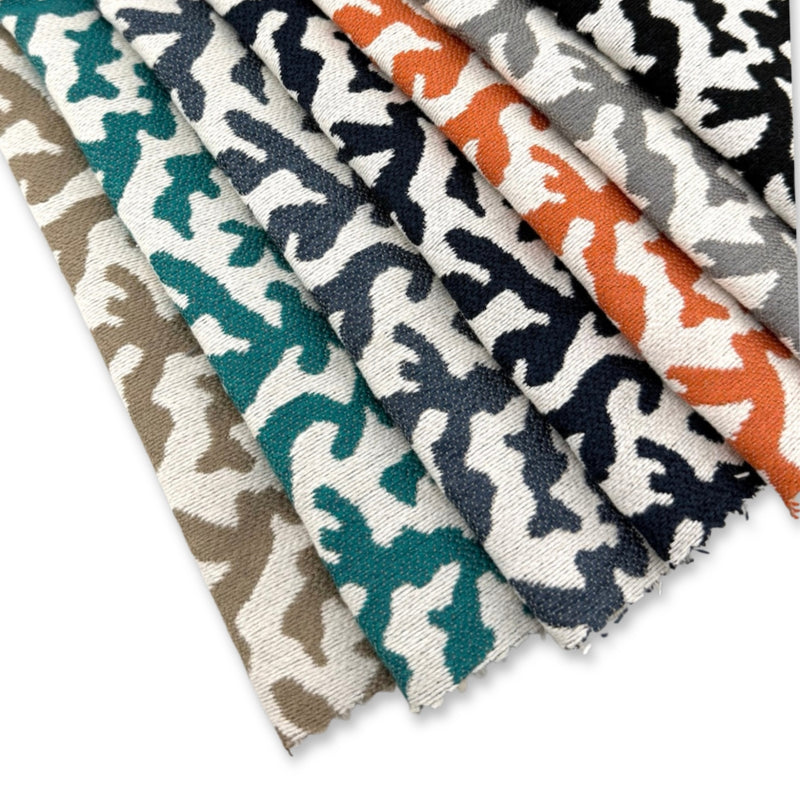 Assorted Revolution Performance Upholstery Fabric swatches in the Sponge pattern arranged in a fanned layout. Each swatch displays the Sponge pattern’s organic abstract motif with subtle tonal variation across neutral, teal, navy, orange, grey, and black colorways, highlighting the fabric’s textured weave and durable performance qualities.