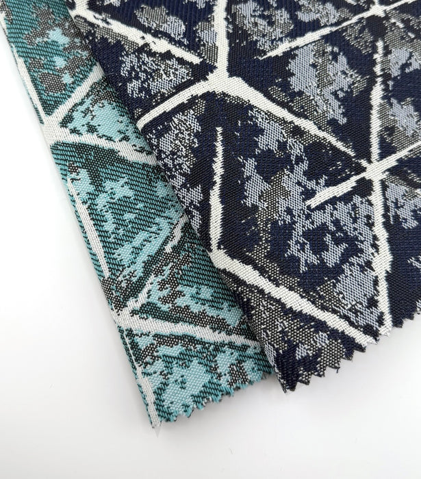Revolution Performance Fabric swatches featuring the Sarong pattern in Navy and Teal colorways, stacked to showcase geometric cube motifs with layered tonal texture and ivory linework for modern, durable upholstery applications.