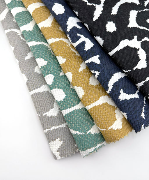 Revolution Performance Fabric swatches in the Janus pattern, arranged in a fanned layout and showcasing multiple colorways including Chrome gray, Water teal, Straw gold, Navy blue, and Carbon black, each featuring ivory abstract organic motifs woven into a durable, high-performance upholstery fabric.