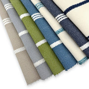 Assorted Revolution Performance Upholstery Fabric swatches in the Starboard stripe pattern, arranged in a fanned layout and showcasing multiple colorways including ivory, navy, sky blue, grass green, overcast gray, and natural beige, featuring crisp vertical stripes woven into a durable, high-performance textured fabric suitable for indoor and outdoor upholstery applications.