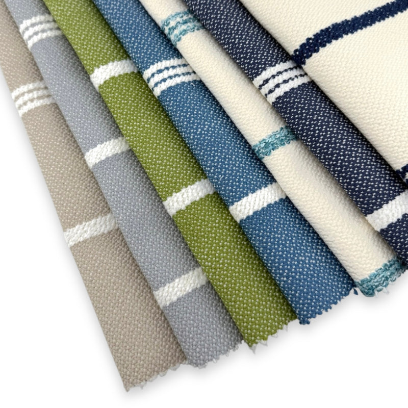 Assorted Revolution Performance Upholstery Fabric swatches in the Starboard stripe pattern, arranged in a fanned layout and showcasing multiple colorways including ivory, navy, sky blue, grass green, overcast gray, and natural beige, featuring crisp vertical stripes woven into a durable, high-performance textured fabric suitable for indoor and outdoor upholstery applications.