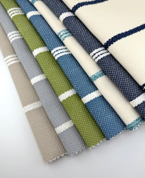 Assorted Revolution Performance Upholstery Fabric swatches in the Starboard stripe pattern, arranged in a fanned layout and showcasing multiple colorways including ivory, navy, sky blue, grass green, overcast gray, and natural beige, featuring crisp vertical stripes woven into a durable, high-performance textured fabric suitable for indoor and outdoor upholstery applications.