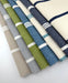 Assorted Revolution Performance Upholstery Fabric swatches in the Starboard stripe pattern, arranged in a fanned layout and showcasing multiple colorways including ivory, navy, sky blue, grass green, overcast gray, and natural beige, featuring crisp vertical stripes woven into a durable, high-performance textured fabric suitable for indoor and outdoor upholstery applications.
