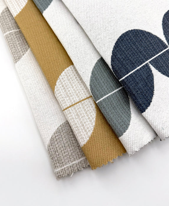 Assorted Revolution Performance Upholstery Fabric swatches in the Lunar pattern, arranged in a fanned layout, featuring modern geometric crescent shapes in coordinated neutral and earthy colorways on an ivory ground, showcasing a woven texture designed for durable, high-performance upholstery applications.